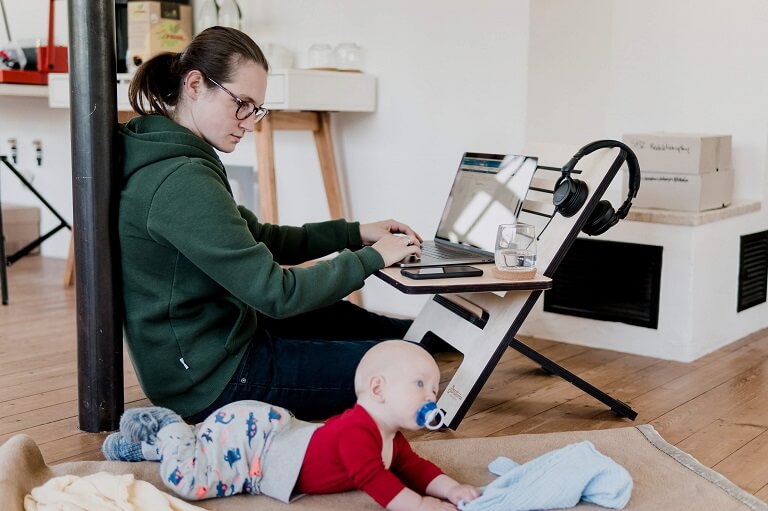 A MOTHER WORKING FROM HOME WHILE MULTITASKING AND LOOKING AFTER HER CHILD.